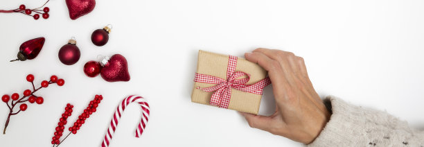 手拿圣诞礼盒在白色的圣诞背景与红色的圣诞装饰品图片下载