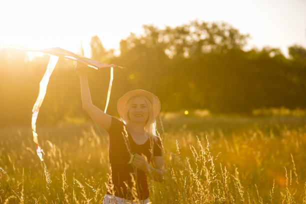 一个快乐的年轻女子，在夏季日落的林间空地上牵着风筝奔跑图片下载