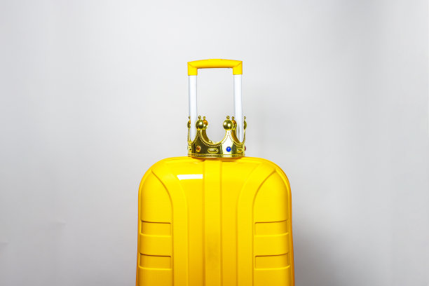 在一个黄色塑料手提箱上，浅色背景上戴着金色皇冠图片下载