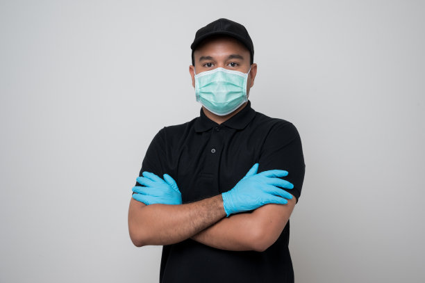 黑色制服递送亚洲男子戴着防护面具和医用橡胶手套，双臂交叉站在孤立的白色背景安全递送概念。图片下载