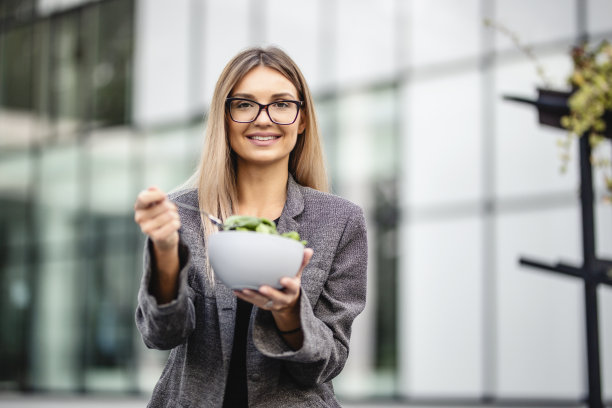 年轻漂亮的女商人在办公大楼前休息，吃午饭，吃新鲜蔬菜沙拉图片下载