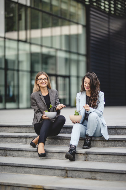 两个年轻的女商人在办公大楼前休息，吃午饭，吃新鲜蔬菜沙拉图片下载