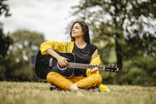 美丽的年轻女子在户外弹奏原声吉他图片下载