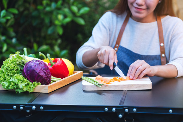 一个女人用刀在木板上切着胡萝卜，盘子里放着各种蔬菜图片下载