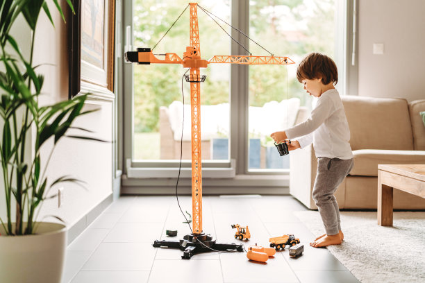 蹒跚学步的小男孩在家里的客厅里玩大型建筑起重机玩具。儿童休闲活动，创造性游戏，运用想象力。图片下载