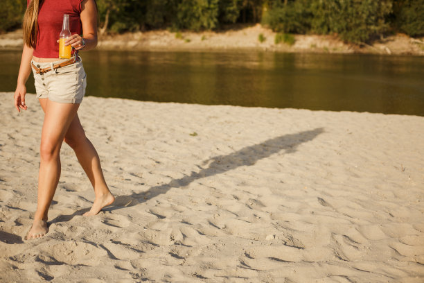 一个年轻女子在海滩上享受清爽饮料的下半部分图片下载