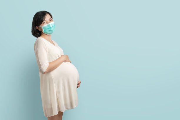 微笑的亚洲孕妇保护面罩触摸她的腹部在蓝色孤立的背景与复制空间图片下载