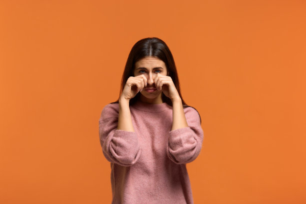 我处理不了。悲伤的美丽的女人在粉红色的毛衣哭泣，擦眼泪，有大问题，与悲伤的表情，哭从绝望，在抑郁。橙色背景图片下载