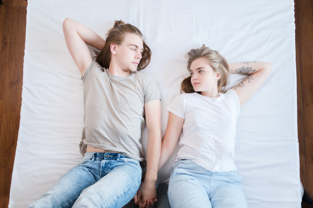 一对年轻的情侣微笑着相爱，一个男人和一个女人躺着，用充满爱意的眼神看着对方。x一代年轻的家庭观念图片下载