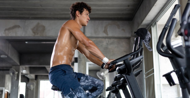 旗帜的白人上身运动男子有氧骑自行车在健身房健身。肌肉发达的人在自行车机上锻炼站锻炼训练。健康生活理念。本空间图片下载