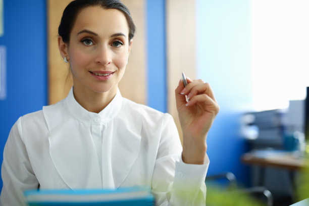 美丽的女商人在白衬衫拿笔和文件在她的手和微笑。图片下载