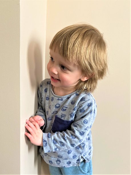 一个皮肤白皙、金发的小男孩躲在一堵墙后面。图片下载