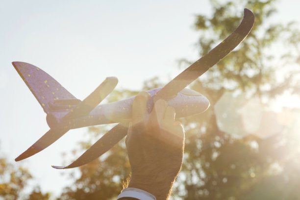 人在夕阳中玩着玩具飞机，梦想着旅行。手用小飞机靠近。玩具飞机-旅行和梦想的象征图片下载
