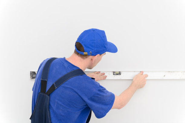 一个穿蓝色工装裤的工人在一堵白色的墙上画线图片下载