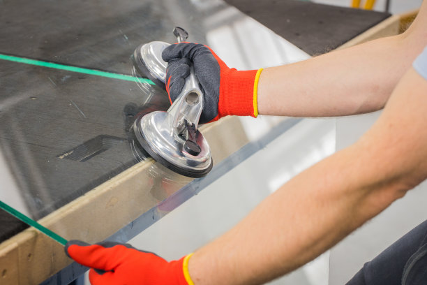 玻璃匠用吸盘做窗户。玻璃制造车间，这个男人用专门的工具抬起桌子上的厚玻璃图片下载