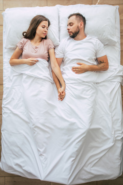 睡觉前。全家人都在睡觉。一对相爱的美丽的年轻夫妇正躺在白色的大床上休息。丈夫和妻子一起在床上。顶视图的照片图片下载