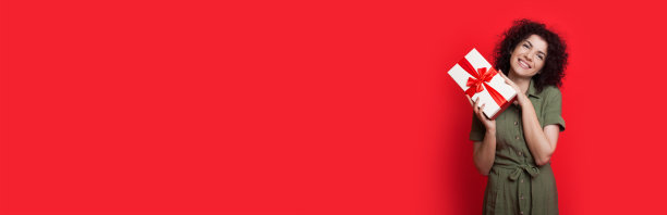 可爱的黑发女人卷头发是在一个包装盒和微笑在相机附近的红色工作室自由空间图片下载