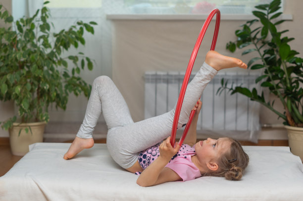 这个女孩在家里是学前班的女孩，从事体操和体育运动。仰卧，用呼啦圈做练习。网上远程学习。闭关锁国则在摧毁隔离。良好的家庭观念图片下载