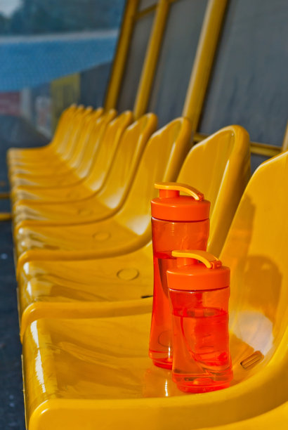 体育场里有很多空座位。座位上有一个橙色的水瓶。喝为运动员。塑料座椅排成一排。风扇座又脏又刮。图片下载
