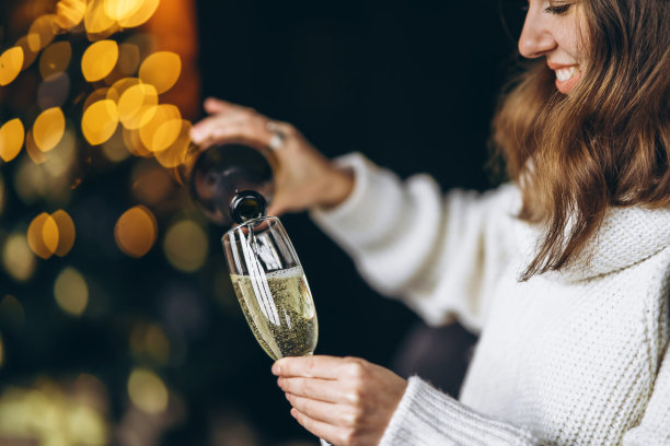 漂亮的女人穿着暖和的毛衣，袜子和圣诞帽，坐在椅子上喝着香槟图片下载