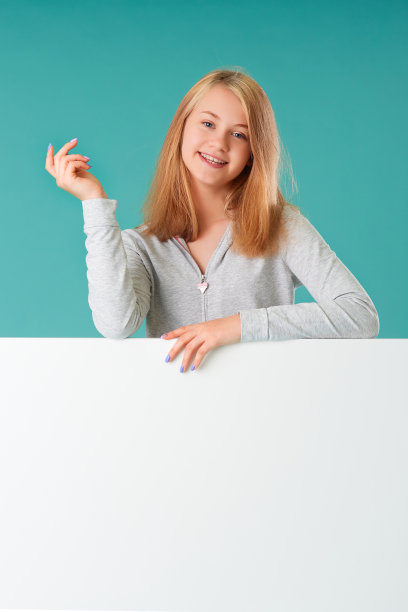 一个美丽的年轻女孩的肖像在一个绿松石背景，站在后面的白色横幅为您的文字图片下载