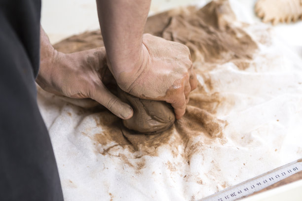 漫步的概念。男工人的手在围裙滚动一块湿粘土在成型前的桌子上的特写。水平的作文图片下载