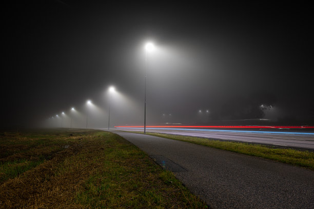 在浓雾的夜晚，汽车灯光长时间暴露在一条孤独的道路上图片下载