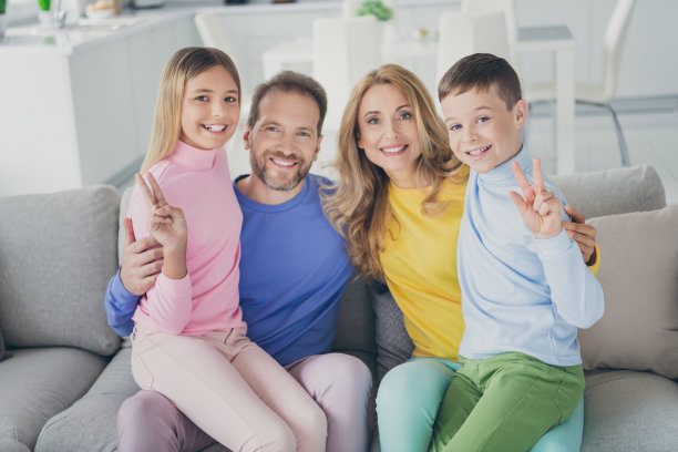 正面家庭的照片两个小男孩男孩女孩坐在妈妈爸爸的膝盖沙发做v手势在屋里室内图片下载