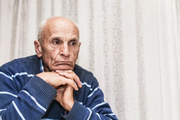 孤独的老人双手抱头坐在床上，悲伤地看着图片下载