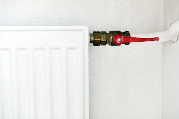 公寓里的白色散热器。散热器。白色暖气片，带有水龙头，可关闭向暖气片供应的水。图片下载