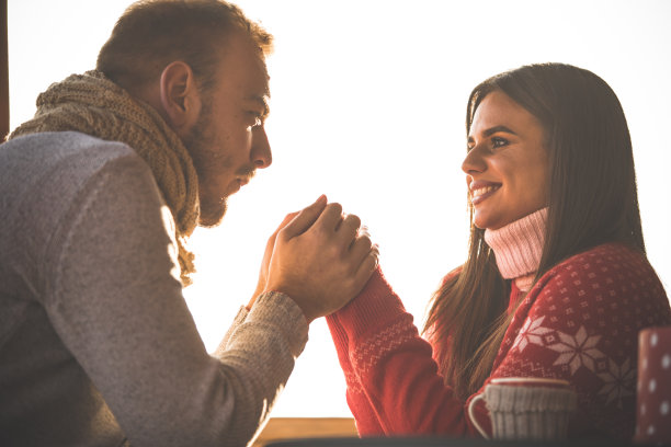 在一个阳光明媚的冬日里，当他的女朋友坐在户外时，一个深情的年轻人正在暖手图片下载