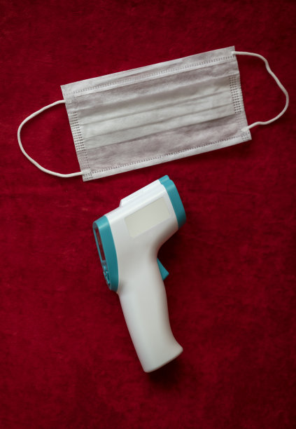 红色背景上的红外线温度计和防护口罩图片下载