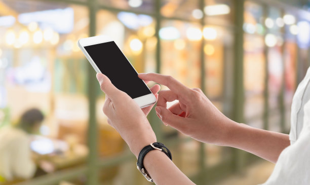 一个女人牵着智能手机，黑屏在模糊的购物中心室内背景上发短信或做广告。模拟手机的概念。图片下载