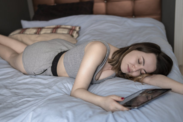 美丽的年轻女子在床上睡觉，手里拿着电子平板电脑图片下载