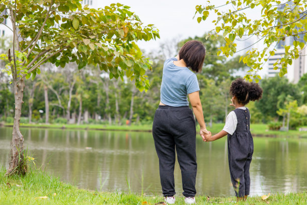 后视图快乐的混血家庭单身母亲和小女儿手牵着手，一起在公园里散步。父母与可爱的孩子女孩享受和有乐趣的夏季户外周末假期图片下载