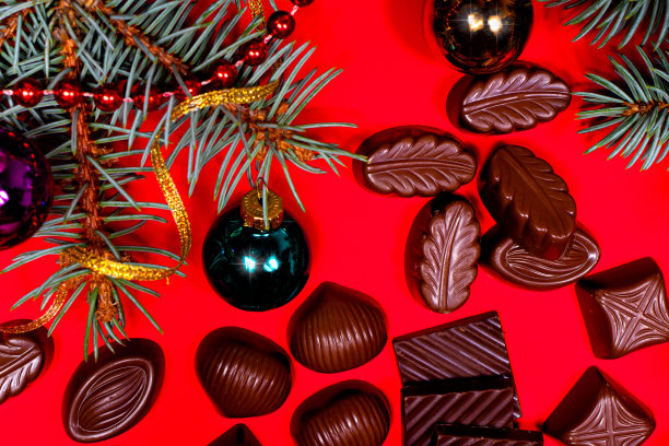 红色新年背景上的巧克力和糖果，云杉树枝和球，还有文字的地方。甜蜜的圣诞礼物图片下载