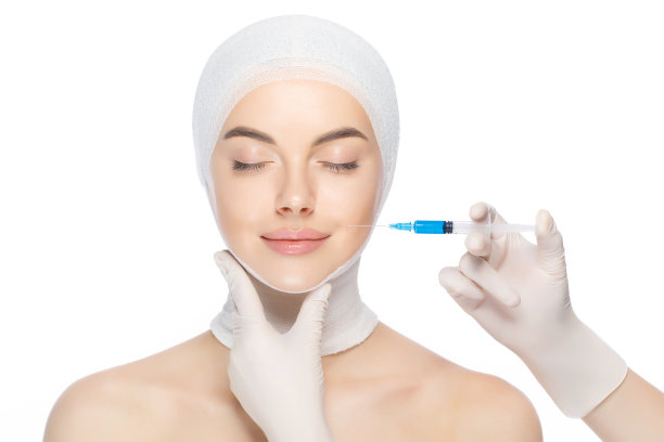 年轻美丽的女子与头部包裹，准备注射器注射到皮肤由美容师闭上眼睛，孤立在白色背景。图片下载