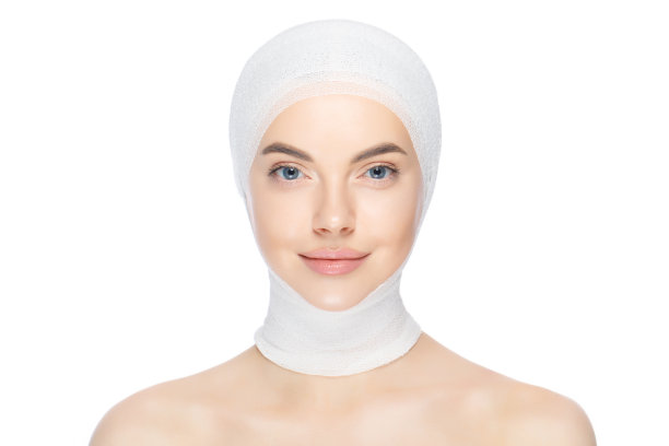 年轻美丽的女子站在医疗绷带，准备整形手术，孤立在白色的背景图片下载