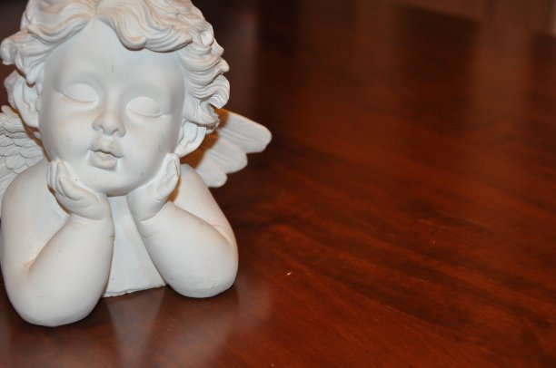 白色天使小雕像躺在棕色的桌子上图片下载
