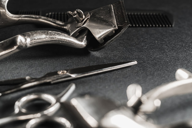 在黑色的表面上是旧的理发工具。老式手工理发器，梳子，剃须刀，美发剪刀。黑色的单色。特写镜头。理发店的背景。对比的阴影。水平图片下载