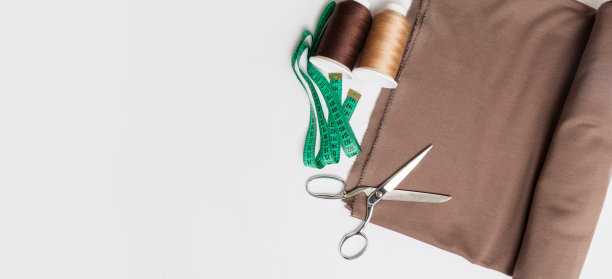 裁剪。缝纫和针线活的配件。剪刀，卷尺，棕色线轴和白色底布。顶视图,flatlay。图片下载