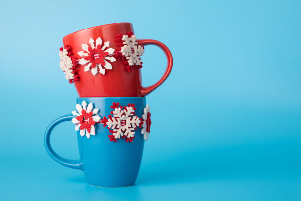 照片中的两个红色和蓝色与雪花装饰的杯子孤立地站在蓝色灯光柔和的背景图片下载