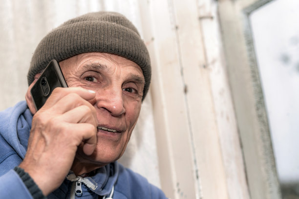 老人的肖像戴着帽子通过电话白色的窗户背景说话图片下载
