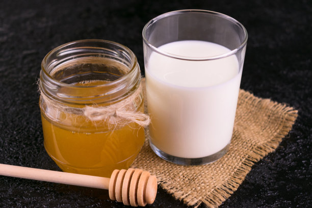一杯牛奶和蜂蜜在黑色的背景。特写镜头。图片下载