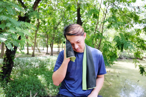 年轻的亚洲运动员在运动和在花园跑步或慢跑后放松和拿着织物擦拭脸上的汗水。图片下载