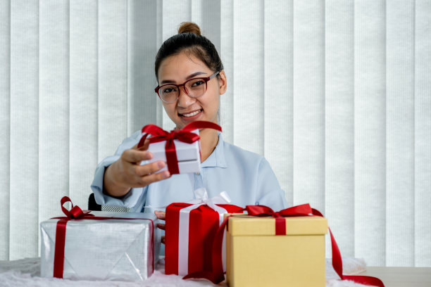 身穿蓝色衬衫的女子拿着一个用红色丝带系着的白色礼盒，礼物是为圣诞节、情人节等特殊节日准备的图片下载
