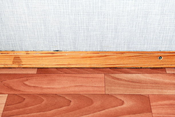铺有油毡的地板和饰有刨花板的墙壁之间的木制踢脚板图片下载