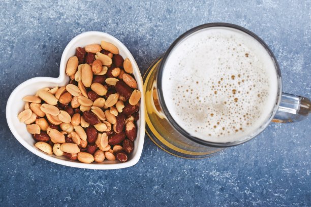 心形碗里的花生，蓝色背景上的啤酒图片下载