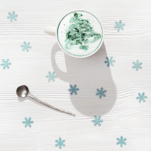 俯视图的一杯咖啡卡布奇诺与图案新年树在白色木桌装饰蓝色雪花。图片下载