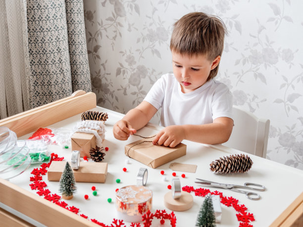 孩子们用牛皮纸包裹手工制作的圣诞礼物，里面有彩色的绒球和雪花丝带。孩子为庆祝新年准备礼物。寒假前的宁静休闲活动。图片下载